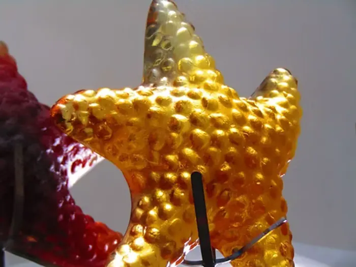 A cast glass starfish with a golden, textured finish, mounted on its steel stand